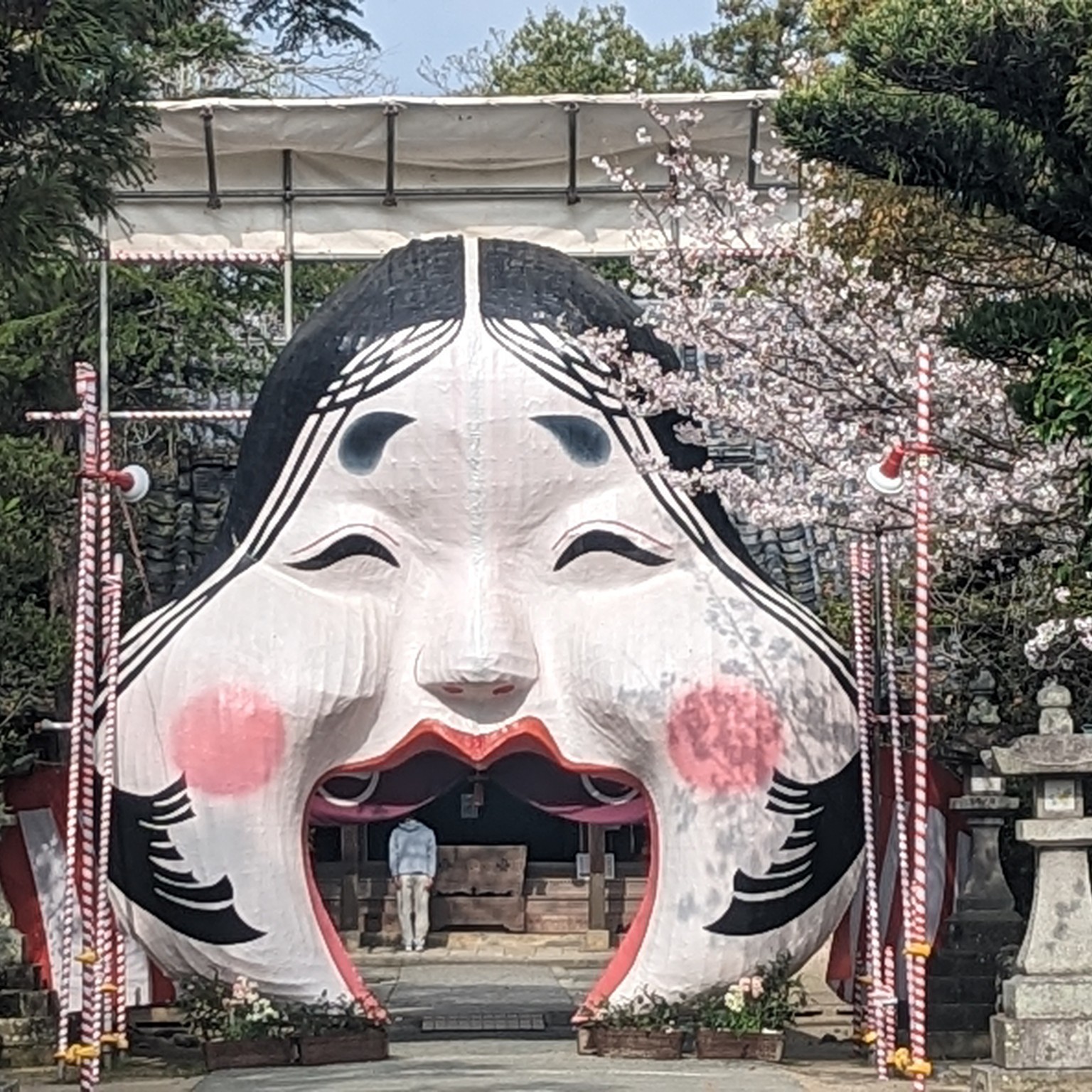 桜に囲まれ、口を大きく開けて迎える日吉神社のお多福さん