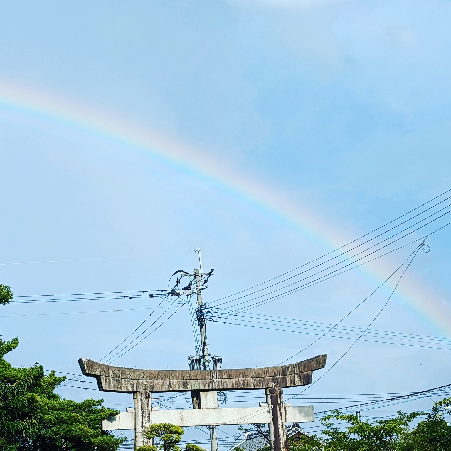 日吉神社の石の鳥居の上、青空にかかる淡い虹